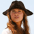 Pixelated image of a person with long brown hair wearing a dark wide-brimmed hat and a white top against a light background.