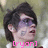 A pixelated image of a person with dark hair and purple eyeshadow, wearing a white top, with pink text at the bottom.