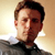 Pixelated static image of a person with short brown hair wearing a dark shirt against a light gradient background.