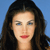 Pixelated close-up of a person with long dark hair against a solid blue background, showing light skin tone, blue eyes, and red lips.