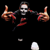 Pixelated static icon of a skeletal figure with outstretched arms, red accents on limbs and torso, and scattered white fragments against black background.