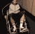 A person in a wheelchair wearing light-colored jacket and dark pants, with visible white socks and shoes.