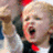 Pixelated image of a person with light hair wearing red and black clothing, mouth open in an expressive gesture.