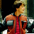 Pixelated static image of a person in an orange jacket with red tie and dark hair, standing against a dark background with greenish elements.