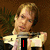 A person with light brown hair in a white shirt holds up three different text displays: a single red vertical line, '<333', and 'David' in red pixelated font.
