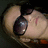 A pixelated image of a person wearing dark sunglasses with visible reflections, positioned on the left side against a black background.