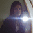 Pixelated image of a person with dark hair holding a bright light source, wearing a dark hooded garment against a muted background.