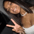 A pixelated image shows a person with long dark hair wearing a white sleeveless top, making a peace sign gesture with their right hand.