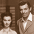 Two people in a sepia-toned pixelated image with a blurred background, one in a light shirt and the other in a collared shirt with a tie.