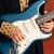 A person plays a blue and white electric guitar with visible hands, fretboard, and body details.