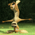 A pixelated figure in a dynamic pose with arms extended horizontally and one leg lifted, set against a dark green background with a lighter green foreground.
