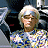 Pixelated static image of a person with light-colored hair wearing a multicolored patterned shirt against dark background elements.