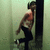 Pixelated image of a person leaning against a dark vertical structure with one leg raised, wearing light-colored top and dark pants.