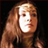 Pixelated static image of a person with light brown hair and fair skin against dark background, wearing dark clothing.
