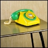 Yellow and green rotary telephone with coiled cord on reflective surface against textured background.