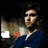 Pixelated image of a person with dark hair wearing a blue top, holding an object with green and orange hues against a black background.