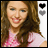 A pixelated image of a smiling person with long brown hair wearing a pink top, next to two heart icons and the name 'Miley' in stylized text.