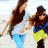 Two pixelated figures in motion, one with long brown hair and light blue pants, the other wearing a dark cap and yellow shorts against a pale background.