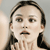 Pixelated close-up of a person with dark hair tied back, light skin, and a neutral expression against a muted background.