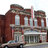 Pixelated static image of a building facade with brown and gray tones, featuring multiple windows and architectural details.