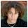 Pixelated static image of a person with light skin tone, brown hair, and dark clothing against a multicolored background.