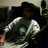 Pixelated static image of a person in dark clothing holding an object with light and brown tones against a muted background.
