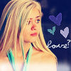 A blonde woman with long hair and a teal strap on her shoulder, looking slightly left with a neutral expression, against a dark background with three hearts and 'love?' text.