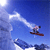 Pixelated static image of a skier in mid-air against a blue sky with white clouds, featuring a red ski and dark clothing on the figure.