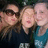 Three people with light skin tones pose closely together in a pixelated image; the central figure has long brown hair and wears dark clothing, while the rightmost person wears blue.
