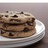 A layered cake slice with chocolate chips on top rests on a white plate against a neutral background.