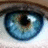 A close-up of a blue eye with visible iris details, accompanied by cyan pixelated text on a brown background describing a romantic interaction between a blue-eyed guy and a brown-eyed girl.