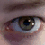 A close-up of a human eye with green-brown iris and visible eyelashes, showing text overlays that change across frames.