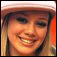 A static pixelated image of a smiling person with light brown hair wearing a white cap, set against an orange background.