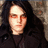 A pixelated image of a person with long dark hair and red eyes, wearing a black coat over a dark shirt against a textured background.
