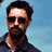 Pixelated static image of a man with dark hair, sunglasses, and beard against light blue background.