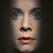 Pixelated close-up of a human face with light skin tone, dark eyebrows, blue eyes, and pink lips against a dark background.