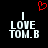 Black background with white pixelated text reading "I LOVE TOM.B" and a red heart symbol above the left side of the text.