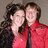 Two people stand close together in a pixelated image; one wears red clothing, the other dark clothing with long hair.