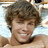 Pixelated close-up of a person with brown curly hair, light skin tone, and visible facial features including eyes, nose, mouth, and chin.