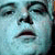 Pixelated close-up of a face with light blue skin tone, dark eyebrows, and a slightly open mouth showing teeth.