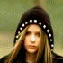 A young woman with long light brown hair wears a black beanie with white dots and a striped hoodie, shown in multiple poses against a blurred green background.