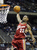 Pixelated image of a basketball player in red jersey shooting a ball toward hoop with backboard and net visible.