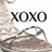 Pixelated image with bold black text 'XOXO' centered above a blurred grayscale figure holding an object.