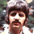A pixelated close-up of a person with dark hair and a mustache, wearing a light-colored shirt against a blurred background.