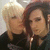Two people in black shirts pose closely together, one with light blonde hair and the other with dark red hair, in a static image with no visible text.