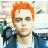 A static image of a person with orange hair wearing a blue jacket over a white shirt against an indistinct background.