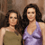 Two women with long dark hair stand side-by-side against a brown textured background, one in a green sleeveless top, the other in a purple sleeveless top.