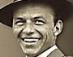 Static grayscale image of a smiling man wearing a wide-brimmed hat and collared shirt, cropped to show upper face and shoulders with visible pixelation.