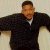 A pixelated figure in a black jacket and white shirt with arms extended against a light background.