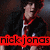 Pixelated image of a person in dark clothing with red accents, holding an object near their face against a dark background.